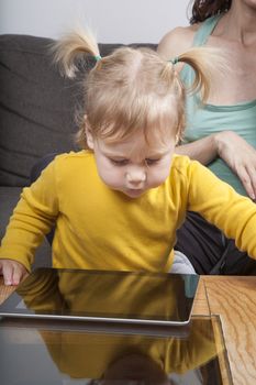 nineteen month aged blonde baby yellow shirt with pigtails looking at blank screen tablet on brown table