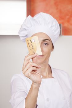 credit card with chip in hand of brunette happy chef woman with professional jacket and hat in white and orange kitchen