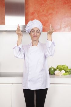 portrait of brunette happy chef woman with professional jacket and hat black trousers in white and orange kitchen