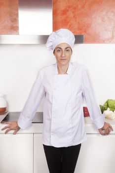 portrait of brunette chef woman with professional jacket and hat black trousers in white and orange kitchen