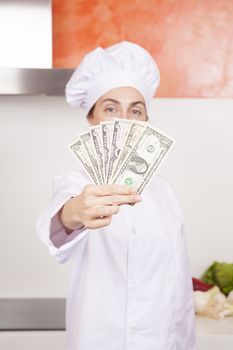 wad of one five and ten Euro banknotes wad in hands of brunette happy chef woman with professional jacket and hat in white and orange kitchen