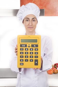 portrait of brunette happy chef woman with professional jacket and hat in white and orange kitchen showing blank screen big yellow calculator with large numbers