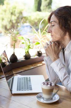woman with white shirt in front of keyboard pc laptop and cappuccino coffee cup ready thinking on light brown wooden table