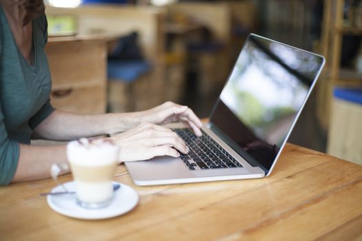 woman with green shirt typing on keyboard pc laptop and cappuccino coffee cup ready thinking on light brown wooden table