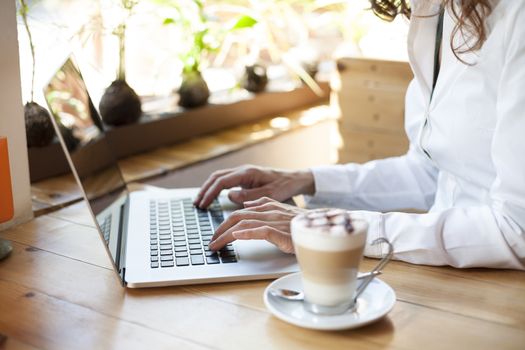 woman with white shirt typing on keyboard pc laptop and cappuccino coffee cup ready thinking on light brown wooden table