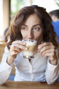 portrait of woman with white shirt drinking cappuccino coffee cup in hands on light brown wooden table cafe
