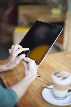 woman hands touching digital tablet blank screen with cappuccino coffee cup on light brown wooden table cafe