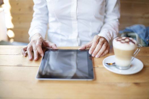 woman touching digital tablet blank screen with cappuccino coffee cup on light brown wooden table cafe