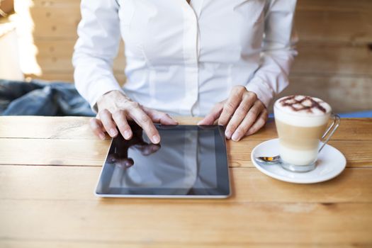 woman touching digital tablet blank screen with cappuccino coffee cup on light brown wooden table cafe