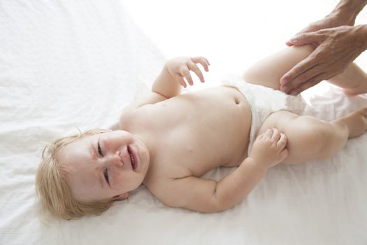 one year blonde baby naked crying over white bedcover with mom arms
