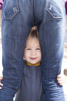 blonde nineteen month age baby with blue and yellow dress between mother blue jeans back woman legs looking at camera