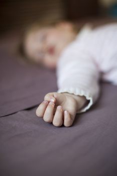 closeup hand of blonde caucasian baby nineteen month age with pink and white stripped jersey sleeping on brown sheets king bed