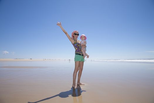 happy woman with sunglasses green shorts headscarf and baby pink hat in arms at beach Conil Cadiz Spain