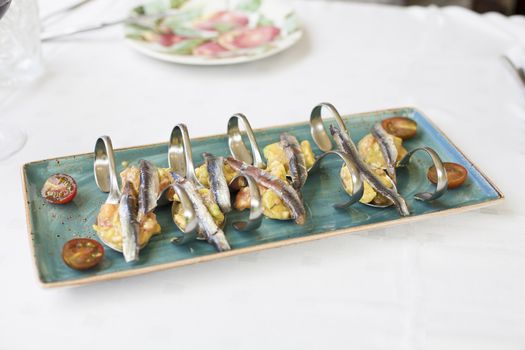 still life of ceramic green dish tray with delicious anchovies with guacamole and tomato in metal curved spoons on restaurant white table