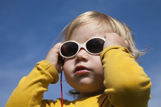 portrait of two years aged blonde happy baby yellow shirt with white kid sunglasses and blue sky background