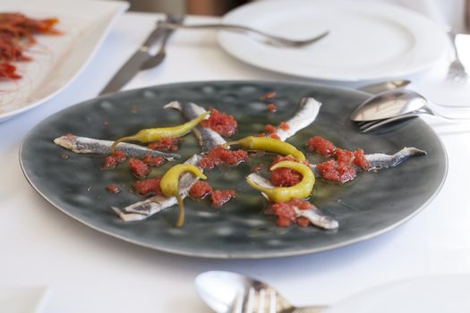 still life of dark grey dish with delicious sardines like anchoas with tomato and chilli on restaurant white table