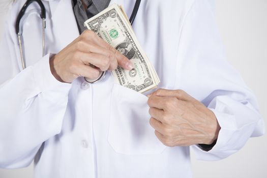 woman doctor hands with white gown and stethoscope tucking a wad of dollar banknotes in her pocket