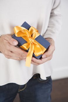 blue gift box with yellow ribbon in woman blue jeans cream jersey hands over white background