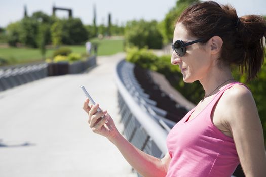 red hair head woman with pink shirt black sunglasses and pigtail reading mobile phone smartphone in park