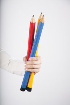 closeup of blue red and yellow primary colours big pencils in woman hand fingers isolated over white background