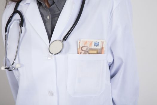 woman doctor with white gown and stethoscope with a wad of Euro banknotes in her pocket