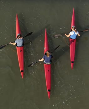 Three female kayakers on the water from above.