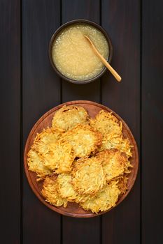 Homemade potato pancakes or fritters on wooden plate with apple sauce, a traditional dish in Germany, photographed overhead on dark wood with natural light