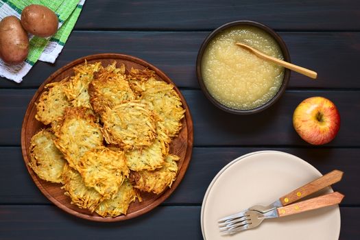 Homemade potato pancakes or fritters on wooden plate with apple sauce, a traditional dish in Germany, photographed overhead on dark wood with natural light