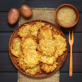 Homemade potato pancakes or fritters on wooden plate with apple sauce, a traditional dish in Germany, photographed overhead on dark wood with natural light