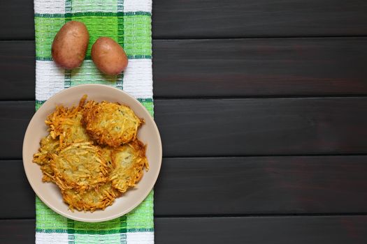 Homemade potato pancakes or fritters on plate, a traditional dish in Germany, photographed overhead on dark wood with natural light