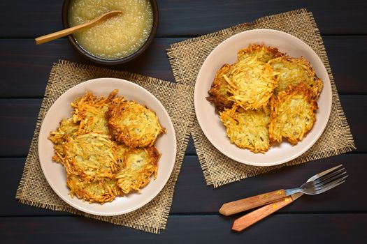 Homemade potato pancakes or fritters on plates with apple sauce, a traditional dish in Germany, photographed overhead on dark wood with natural light