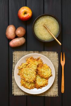 Homemade potato pancakes or fritters on plate with apple sauce, a traditional dish in Germany, photographed overhead on dark wood with natural light