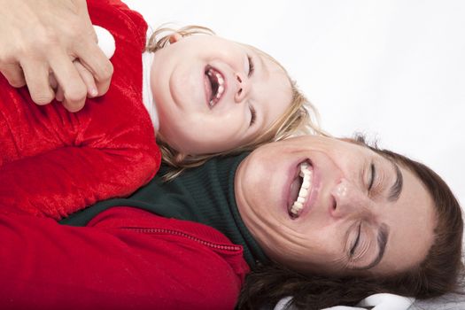 tender and funny portrait of one year age caucasian blonde cute lovely baby Santa Claus Christmas disguise with brunette woman mother red cardigan green sweater embraced laughing together lying on white floor background