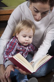 eighteen month aged blonde baby with brunette woman mother reading tale story red book indoor