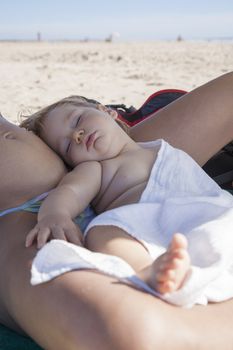 one year baby with white cloth sleeping on mom tummy at beach under parasol