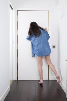 barefoot blue jeans shirt woman back looking to peephole interior house hall white door brown wooden floor