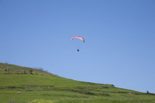 paraglider flying over green field up a beach in Asturias Spain
