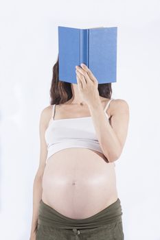 eight month pregnant woman green trousers bare belly stand reading a blue book isolated over white background