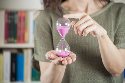 pink sand clock in woman hands over library background