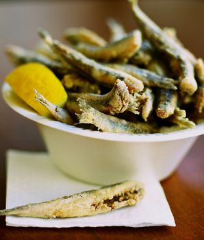 Delicious Deep Fried Small Fish in Bowl with Lemon. Focus on One Fish on Foreground