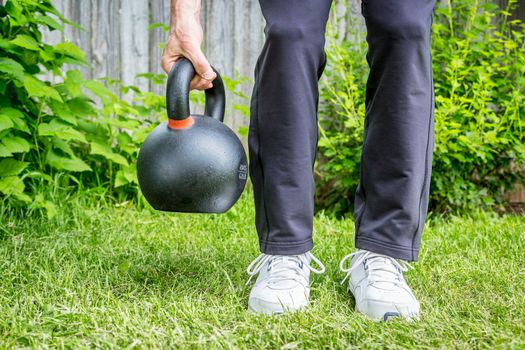 fitness workout with a heavy iron competition kettlebell (62lb/28 kg) on green grass in backyard - outdoor fitness concept