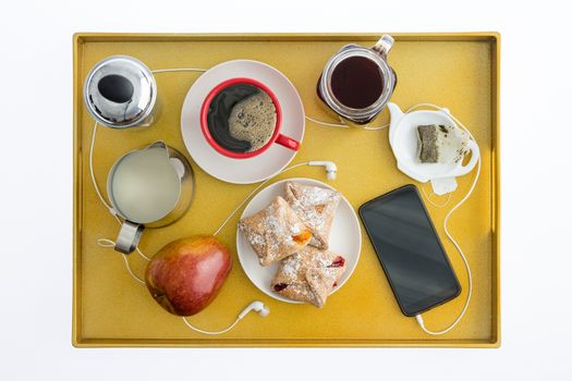 High Angle View of Smart Cell Phone with Earbuds Spread Out on Breakfast Tray with Tea, Coffee, Pastries and an Apple