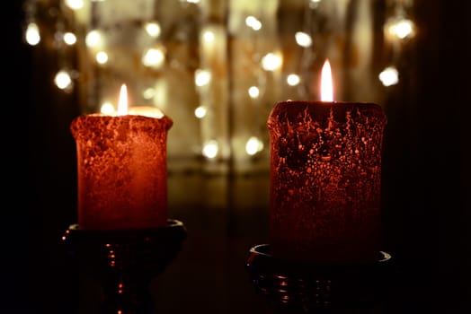 Photo of two orange candles burning over Christmas lights background.