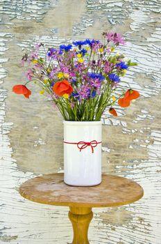 various beautifull summer wild flowers in white vase near old aged wall 