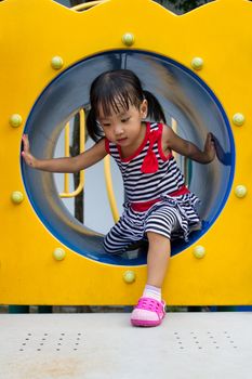 Asian Chinese kid crawling on outdoor playground tube.