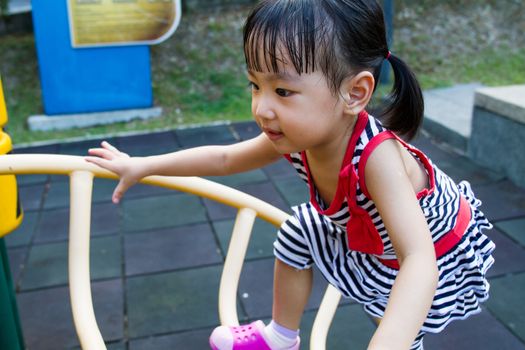 Asian Chinese toddler girl climbing a ladder on the outdoor playground.