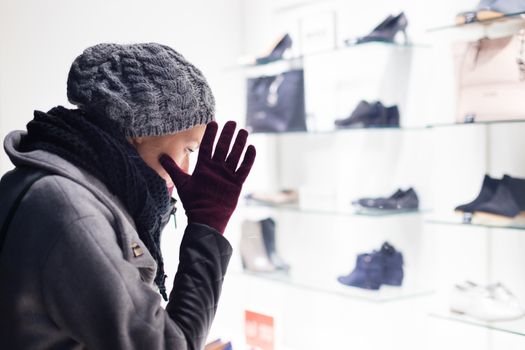 Casualy winter dressed lady window shopping in front of sinfully expensive boutique store dispaly window. Customer woman in shopping street, looking at window, outdoor.