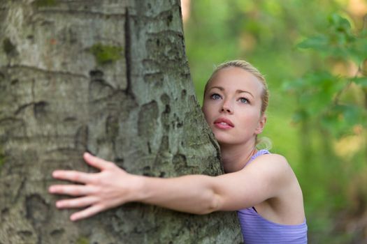 Relaxed young lady embracing a tree receiving life energy from the nature.