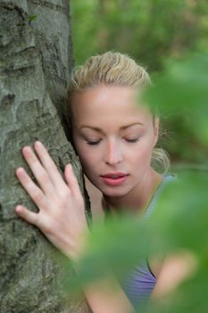 Relaxed young lady embracing a tree receiving life energy from the nature.