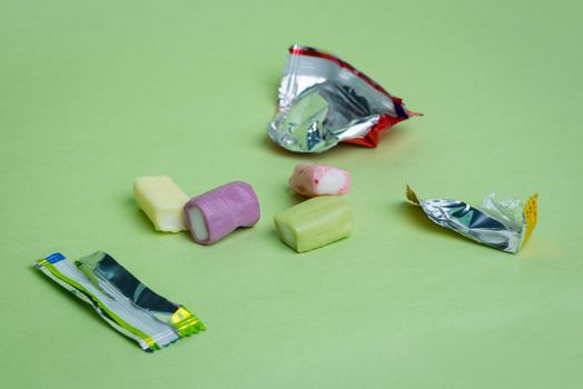 Strawberry, grape, banana and green apple chewy candies and their open wrappers on a green background.